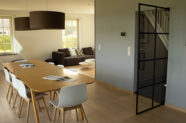 Séjour lumineux avec table à manger, coin salon et porte vitrée en acier dans la maison témoin Sibomat à Bierges