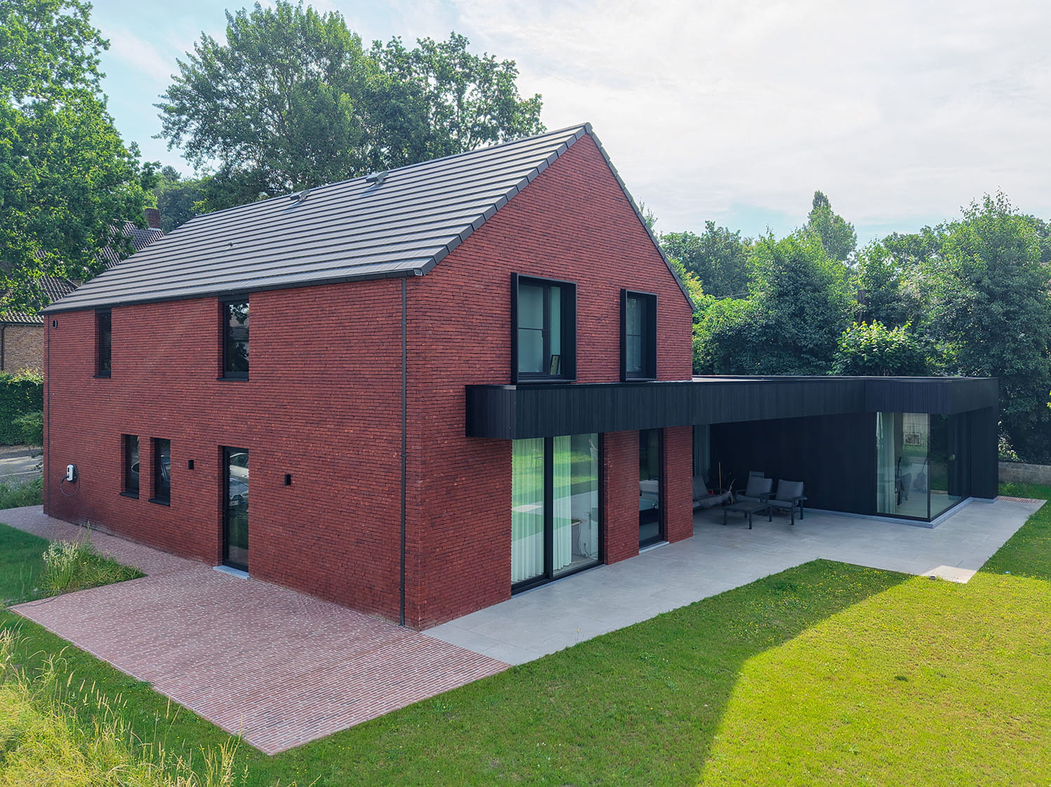 Tuinzijde van moderne woning in Marke met rode gevelsteen, zwarte houten aanbouw en terras