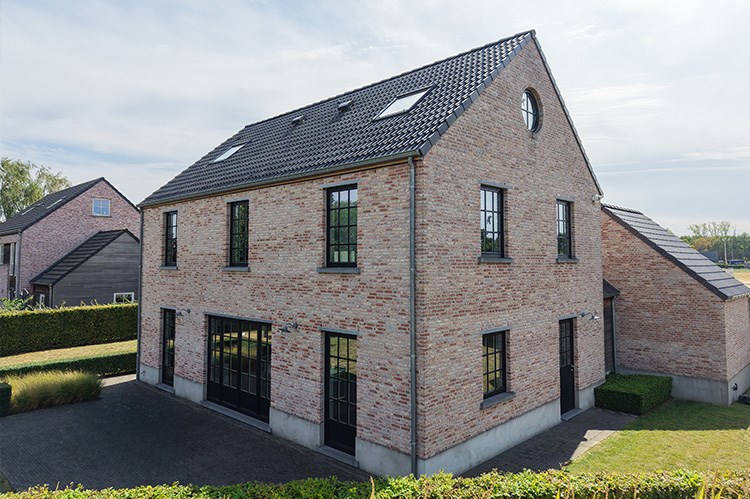 Façade arrière en briques rouges avec grandes baies vitrées et fenêtres de toit de la maison témoin Sibomat à Bierges